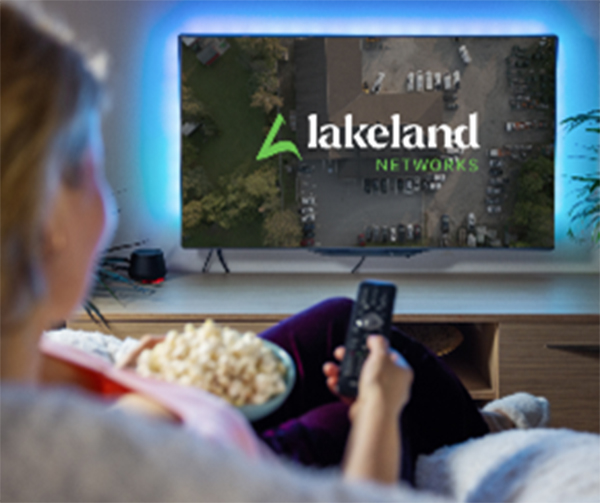Woman on couch holding remote towards TV with Lakeland TV on the screen