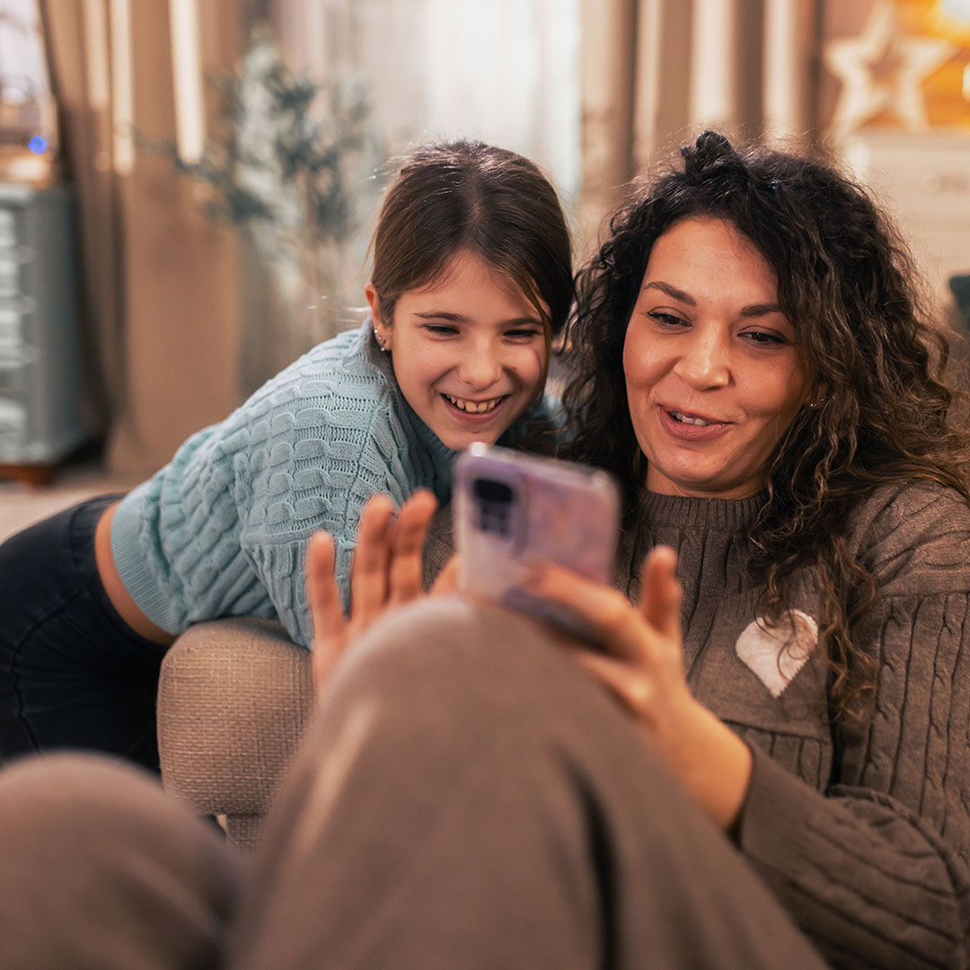 A mother and daughter smile at while viewing a phone screen