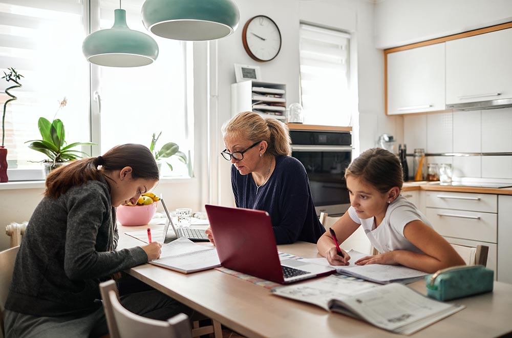 A mother and two daughters sit at a kitchen table doing homework