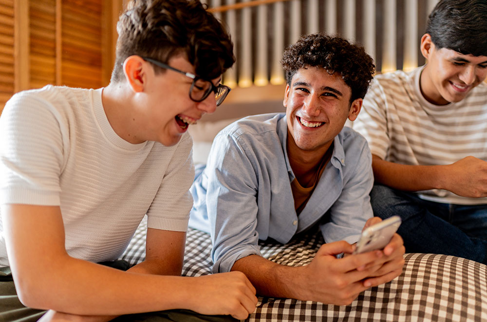 Three teenagers laughing, one on a device
