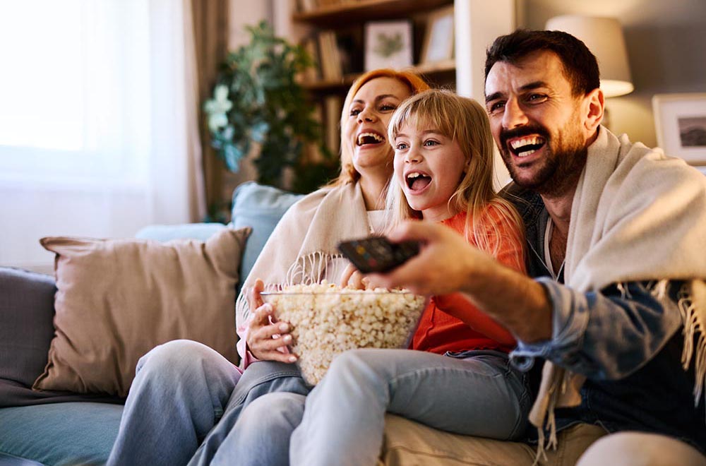 Cheerful family enjoying quality time together while laughing and watching a movie on television, sharing popcorn and cozying up on the sofa in their inviting living room