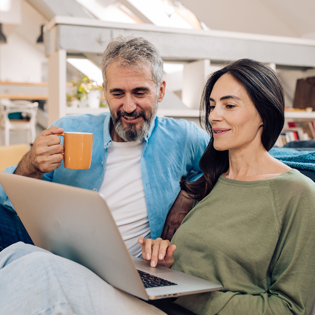 A middle aged couple sitting on a couch looking at a laptop