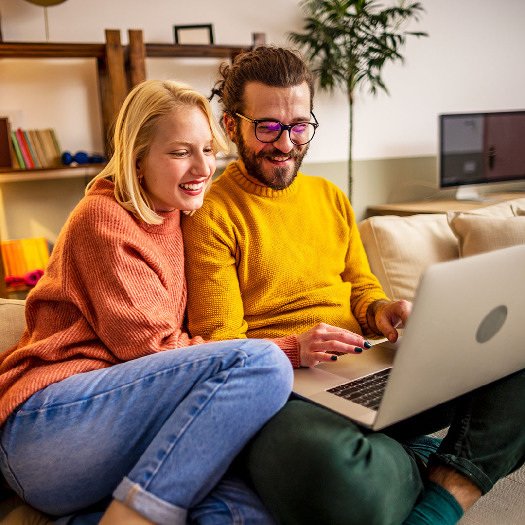 Happy young couple using a laptop while relaxing on a couch at home